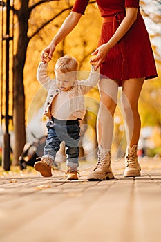 the first steps of the baby. the mother holds son& x27;s hands and teaches to walk.