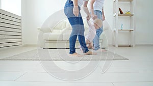First steps of baby toddler learning to walk in white sunny living room. Footwear for child.