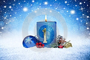 First sunday of advent blue candle with golden metal number red decoration one on wooden planks in snow front of silver panorama