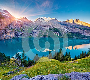 First sunlight gloving mountain hills and meadows. Picturesque summer view of unique Oeschinensee Lake. Sunrise in Swiss Alps with