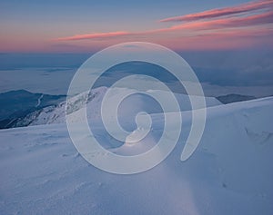 The first sunlight on the mountains shines through the fog and clouds. Snow-covered hills with dramatic scenery.