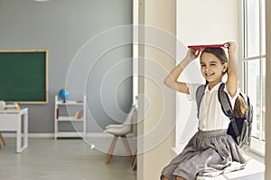 First time at school. Schoolgirl smiles with books in her hands over her head in class.