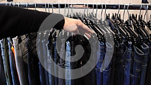 Firsts person view of human hand moves and chooses jeans in clothes store. Trousers for man
