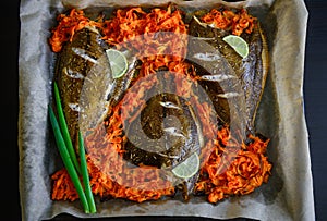 Fish baked on baking sheet with vegetables, close-up. Flounder on parchment with carrots, lime and green onions. Sea fish is a