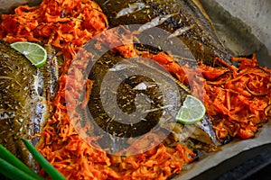 Fish baked on baking sheet with vegetables, close-up. Flounder on parchment with carrots, lime and green onions. Sea fish is a