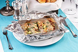Fish baked in a foil with tomatoes, entirely with onion rings, red and green peppers, chili peppers, greens, cheese, mushrooms