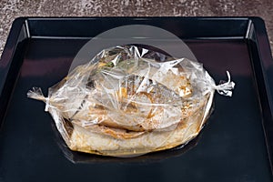 Fish in baking bag. Dorado fish with rice, sauce and herbs wrapped in a baking sleeve in oven ready for cooking. Mediterranean