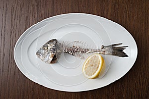 Fish bone left overs with a sliced lemon on a white oval plate.