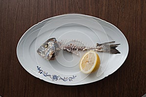 Fish bone left overs with a sliced lemon on a white oval plate.