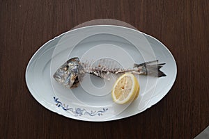 Fish bone left overs with a sliced lemon on a white oval plate.