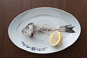 Fish bone left overs with a sliced lemon on a white oval plate.