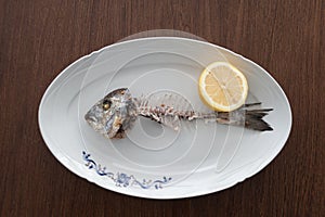 Fish bone left overs with a sliced lemon on a white oval plate.