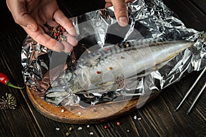 The fish chef prepares Scomber in the hotel kitchen. Before baking, mackerel must be wrapped in foil and spices added