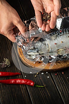 The fish chef prepares Scomber in the hotel kitchen. Before baking, mackerel must be wrapped in foil and spices added