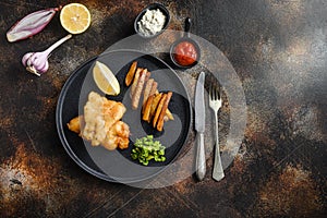 fish and chips with beer-battered cod and fries and a side of tartar sauce and mushy peas on black plate over old rustic metal