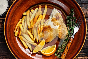 Fish and Chips british fast food with french fries and tartar sauce on a rustic plate. Dark wooden background. Top view