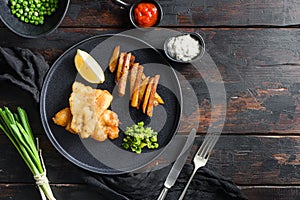 Fish chips with dip and lemon black plate with British traditional cusine food with beer-battered cod and fries and a side of