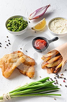 Fish & chips with dip and lemon in a paper cone on white background with all components classic recipe takeaway food  white stone