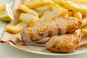 Fish & chips, fried cod or haddock in crispy batter, on a straw paper with a lemon wedge, selective focus