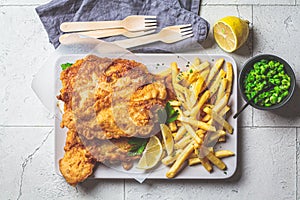 Fish and chips with green peas on gray tile background. British cuisine concept