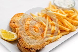 Fish and chips with lemon and sauce on white plate