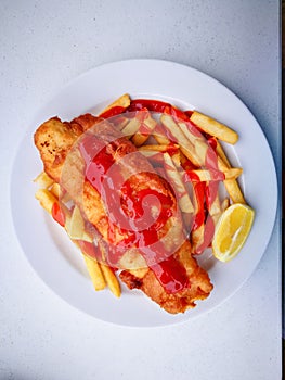 Fish and chips with a lot of ketchup on top in overhead view.