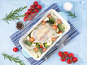 Fish cod baked in blue oven with vegetables - broccoli, tomatoes. Healthy diet food. Blue stone background, top view.