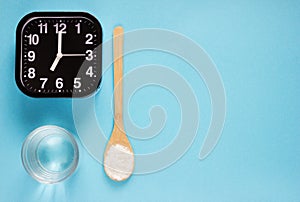 Fish collagen peptides powder and glass of water on blue background. alarm clock near wooden spoon with collagen.