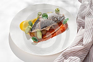 Fish dish - Dorado with rainbow creams. dorado fillet with garnish, greens and lemon on ceramic plate on white