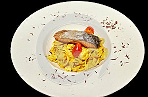 Fish dish: fried or baked salmon with vegetables and pasta on a black background