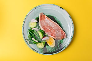 Fish dish - fried fish fillet with vegetable salad. Fresh cucumbers, radish and spinach with fried fish on a plate