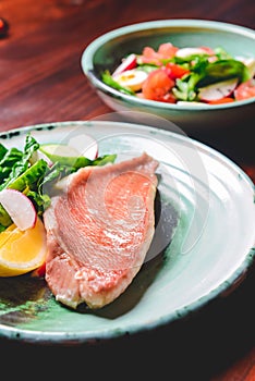 Fish dish - fried fish fillet with vegetable salad. Fresh cucumbers, radish and spinach with fried fish on a plate