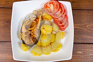 Fish dish - fried trout with potato garnish and tomatoes on a white plate