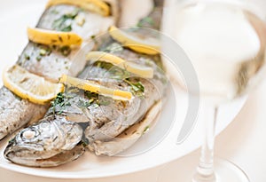 Fish dish on a white plate with glass of white wine.