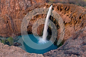 A fish-eye view of Havasu Falls emphasizes the contrasting blue green water against the craggy red rock wall that surrounds it.