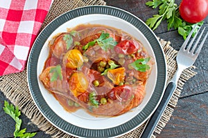 Fish fillet cooked in tomato sauce with green peas and cherry tomatoes on a plate on a wooden background. Healthy eatng concept. E