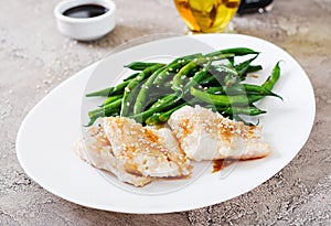 Fish fillet served with soy sauce and green beans in white plate.