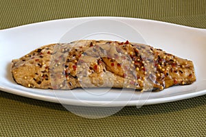 Fish fillet on a white plate on a green background.