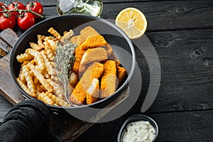 Fish fingers with French fries potatoes, on frying iron pan, on black wooden table background , with copyspace  and space for text