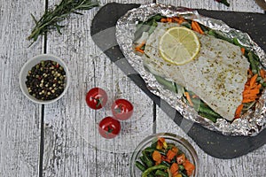 Fish in foil on a stone baked with lemon and vegetables