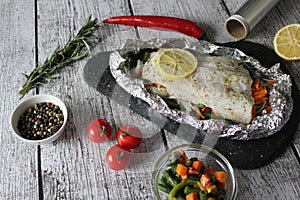 Fish in foil on a stone baked with lemon and vegetables