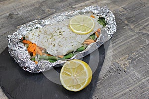 Fish in foil on a stone baked with lemon and vegetables