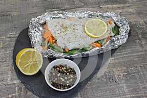 Fish in foil on a stone baked with lemon and vegetables