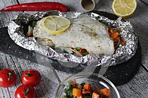 Fish in foil on a stone baked with lemon and vegetables