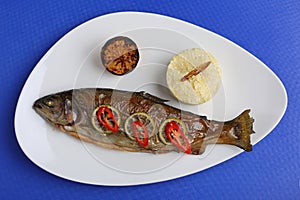 Fish grill dish baked whole grilled on a plate with vegetables and lemon on top