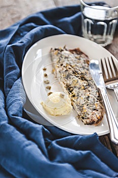 Fish mackerel baked with herbs, mashed potatoes, pesto sauce served on a white plate on a wooden antique background, next to a bl