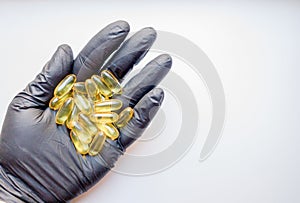 Fish oil capsules in hand in a black medical glove on a white background, the hand takes one tablet from a saucer or plate. Hand