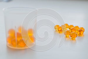 Fish oil capsules in measuring cup on white medical table