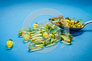 Fish oil capsules with omega 3 and vitamin D in spoon, isolated on blue background. Yellow vitamin pills. Medicine and healthy