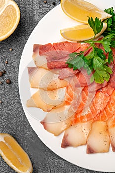 Fish platter salmon and oily fish. On a large white plate. Garnished with a slice of lemon and herbs. View from above. On a gray